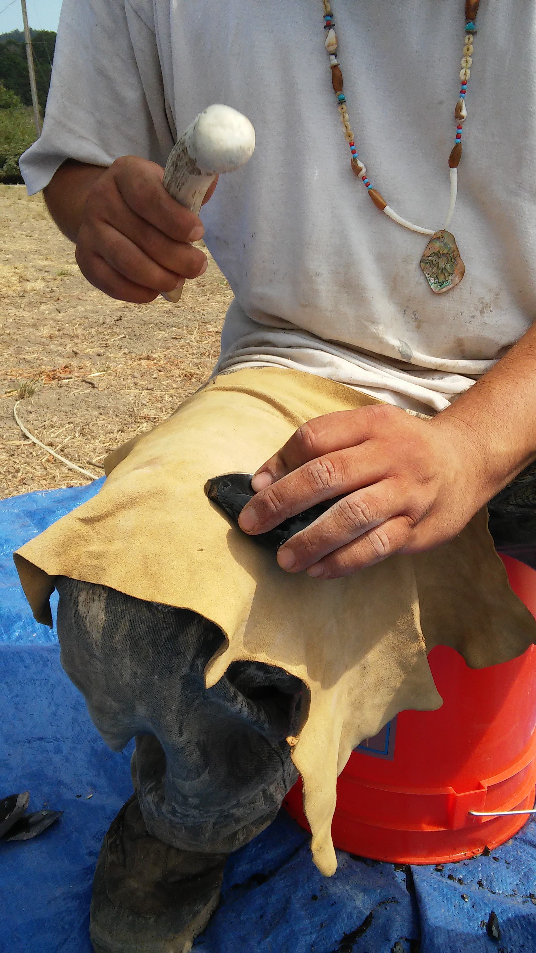 Native Steward Paul Lopez uses an elk antler to flake an obsidian core in an arrowhead-making demonstration. Native Stewards learn and practice traditional crafts and skills at Stewardship Corps, keeping skills like flintknapping alive within the Amah Mutsun Tribal Band.